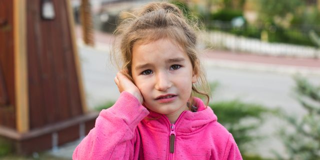 A little girl in a pink hoodie with a sad and tearful face is ho